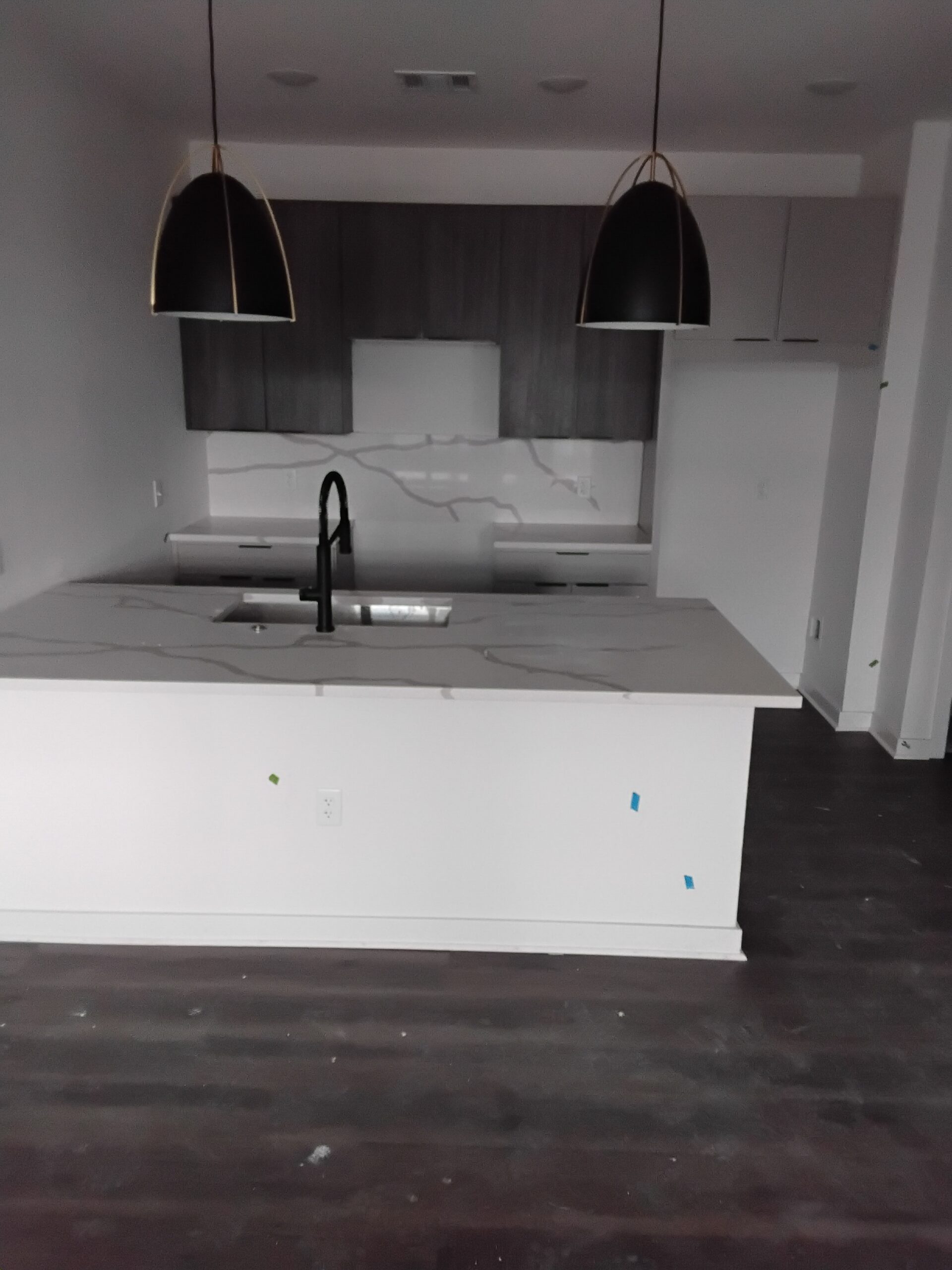Modern kitchen with dark wood cabinets, white marble counters, central island, black faucet and two black pendants. Dark wood flooring.