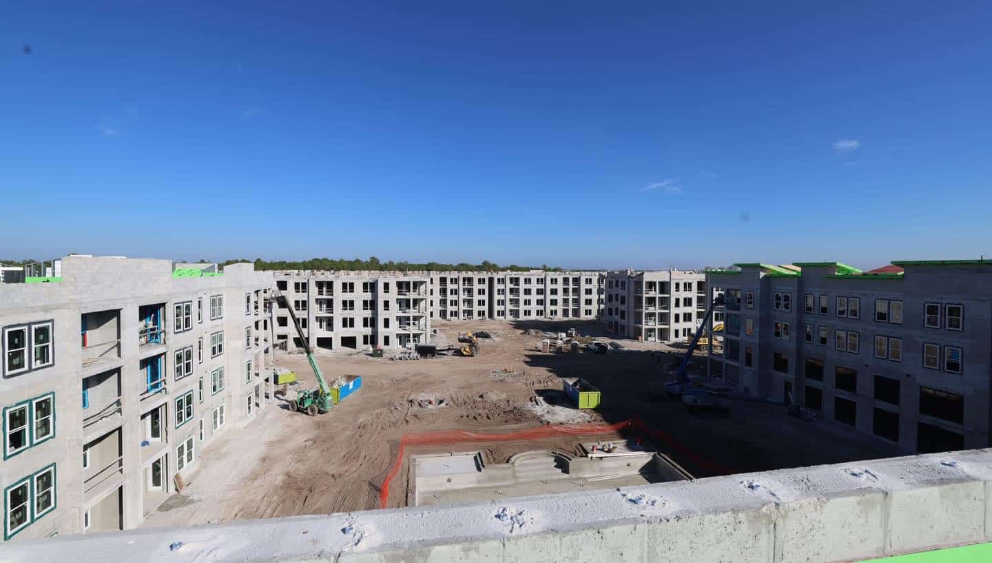 A big construction site featuring several unfinished apartment buildings, scattered equipment, and materials beneath a blue sky.